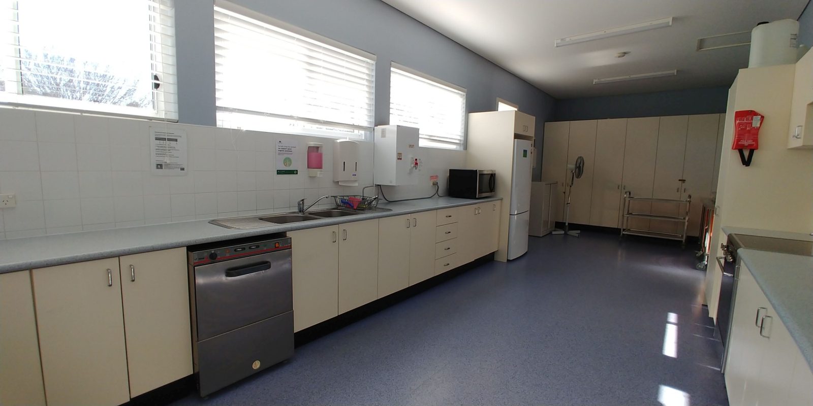 The kitchen with a long bench, double sink, commercial dishwasher, microwave and fridge
