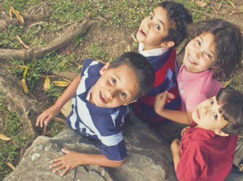 Four smiling children looking up at the camera on the grass
